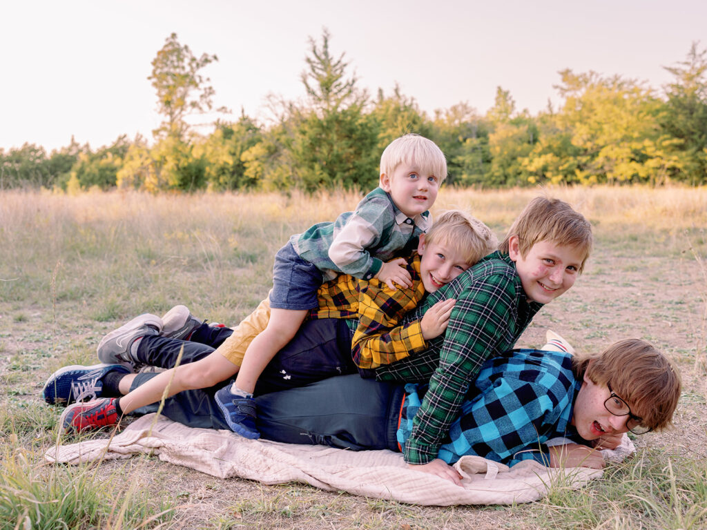 4 young brothers laying on top of eachother in a field