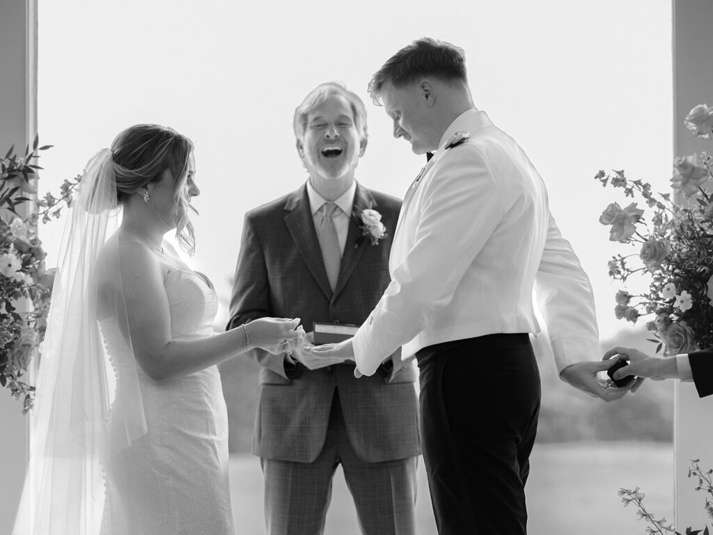 bride and groom exchange rings at the altar as officiant shares a laugh