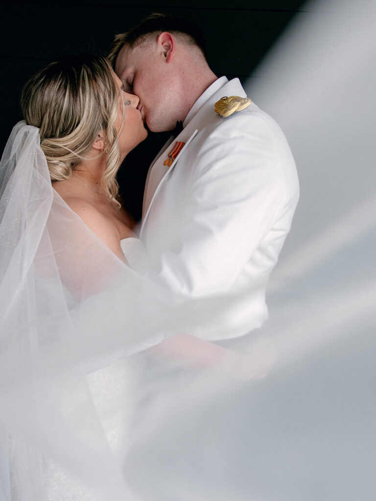 bride and groom kiss in groom suite as veil wraps around them