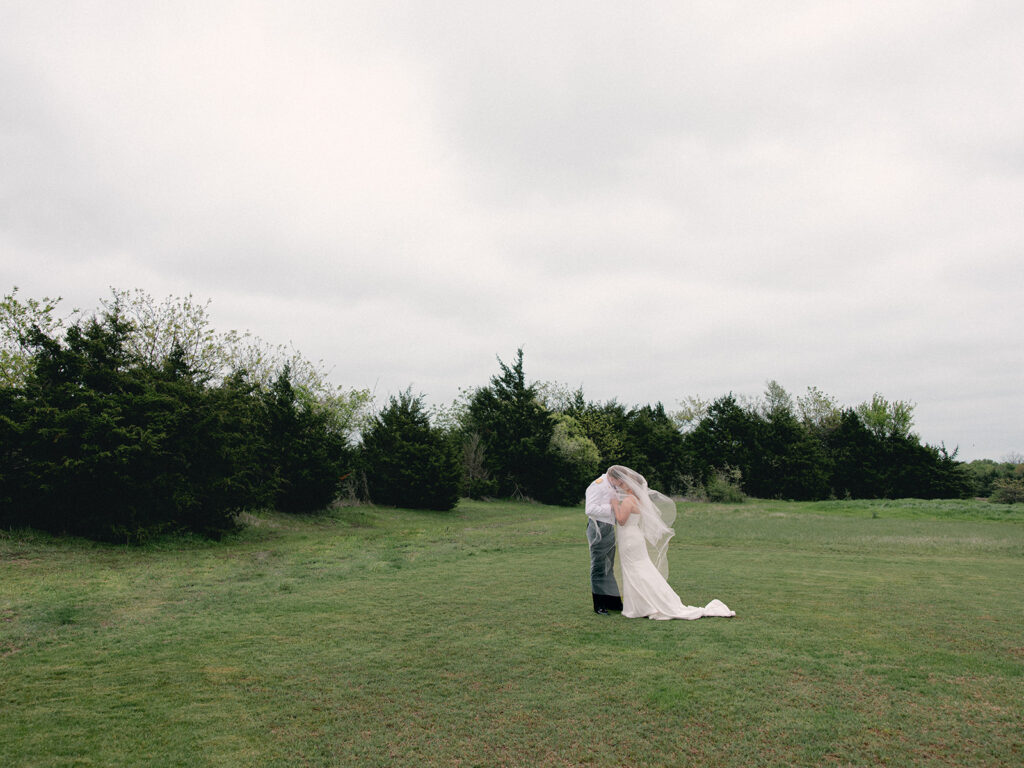 Bride and Groom kiss under the veil after wedding ceremony taking husband and wife photos in a field