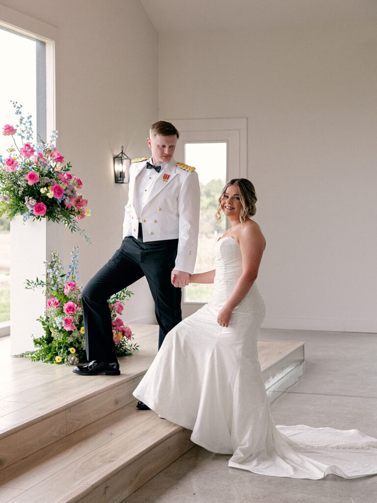groom leading bride up the stairs to their altar surrounded by white walls and colorful florals