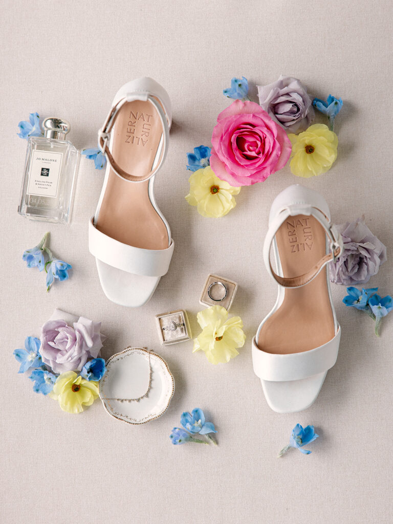 bride's details in styled on a flat lay including her wedding shoes, jewelry and bright wedding flowers