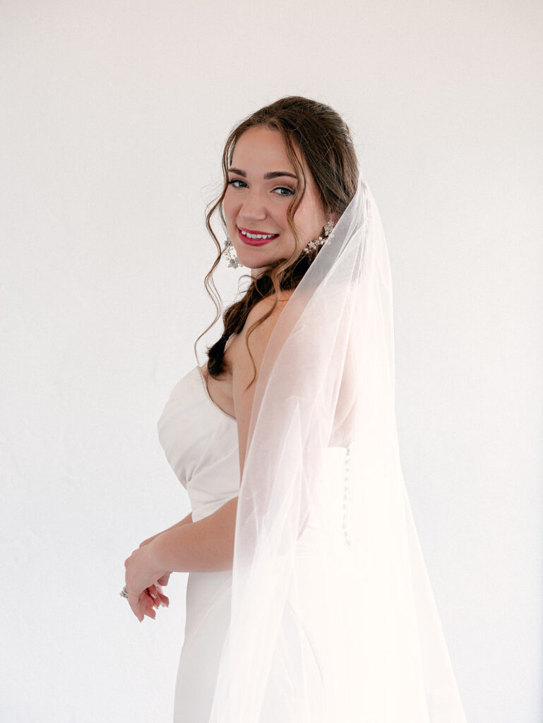 Bride with veil and a white background looking at the camera with a smile
