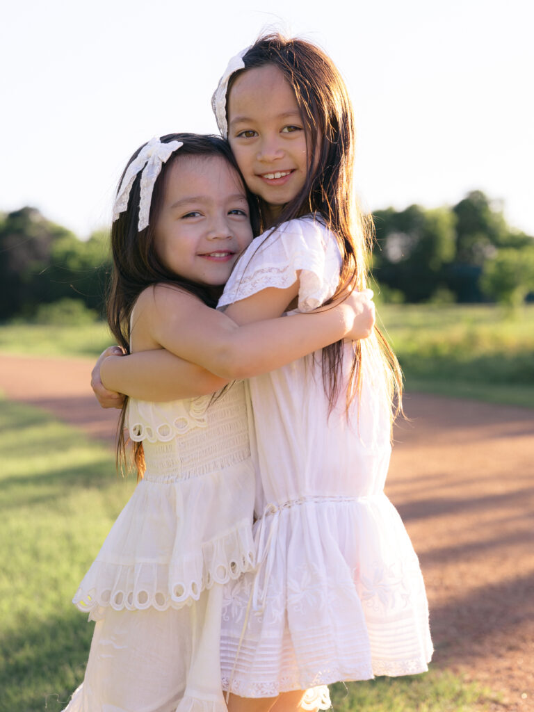 2 young sisters hugging really close smiling at the camera

