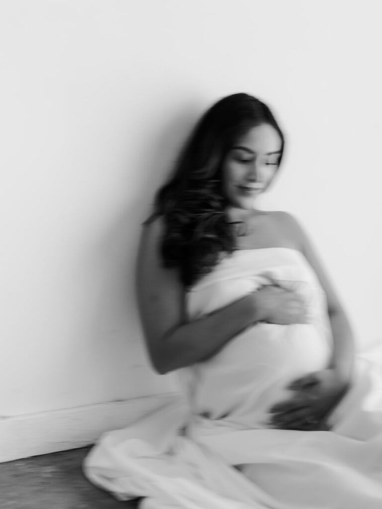 mom holding her pregnant stomach covered in a white bed sheet during a studio maternity session
