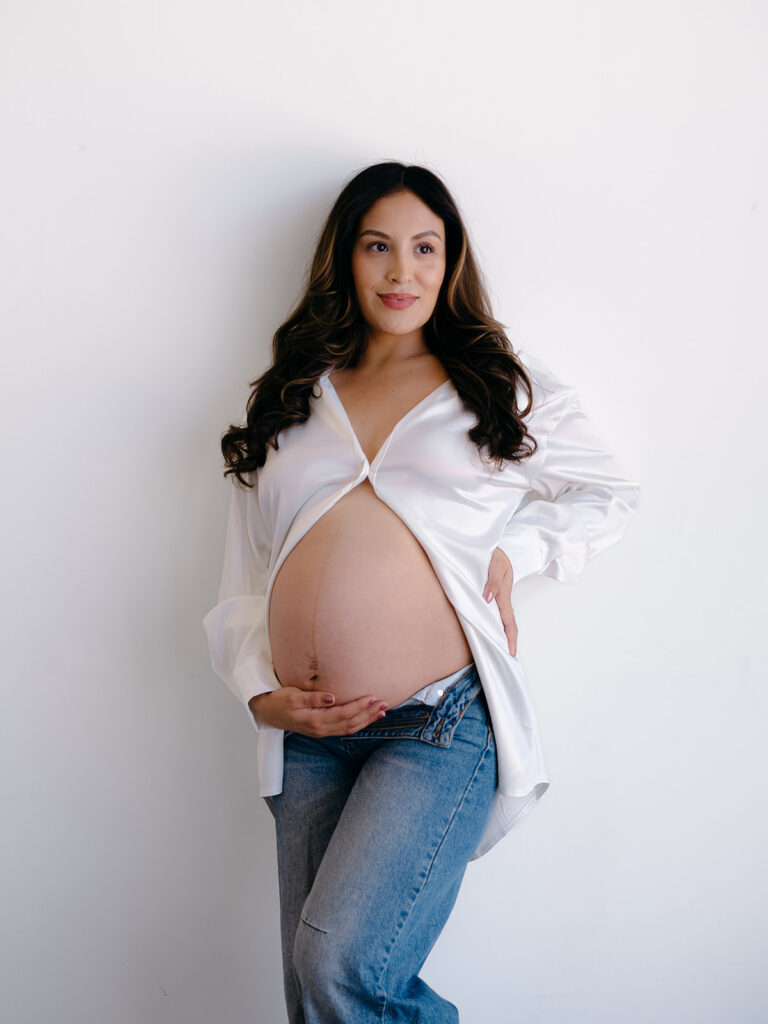 studio maternity session with pregnant belly the feature with a open white button down and undone jeans