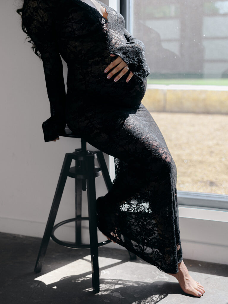 Studio maternity session with a black backdrop and a black lacy dress with mom holding her tummy