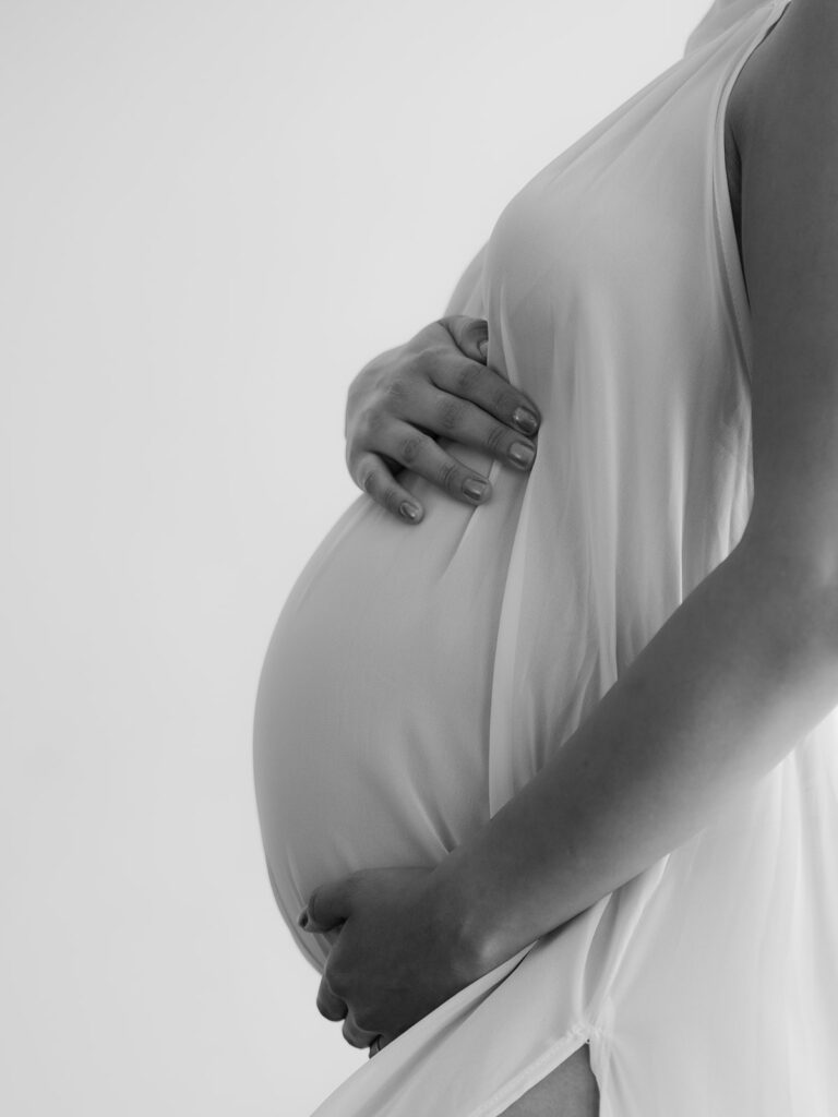 mom holding her pregnant stomach wearing a white flowy gown during a studio maternity session