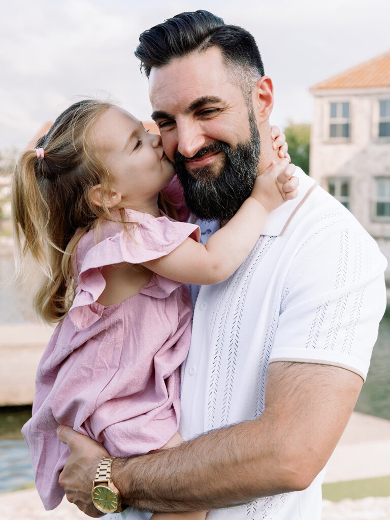 daughter kissing dad's cheek while he holds her

